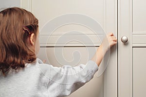 Little girl opens the cupboard. Cute baby girl playing with a wooden cupboard. Toddler baby opens the closet door in the home