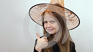 Little girl in orange witch hat showing up big thumb and demonstrating sign of satisfaction. Copy space advertising area