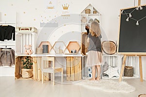 Little girl organizing her toys in white Nordic style bedroom in photo