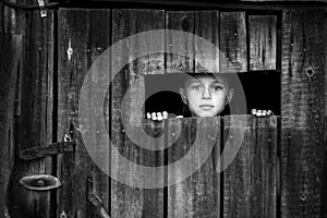 A little girl out peeks anxiously through a crack in the closed door. Black and white photo.