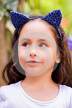Little girl at outdoors on a summer nature, wearing a blue ears tiger accessories over her head in a blurred nature