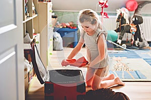 Little girl packing suitcase at home. Cute child putting clothes into suitcase. Preparing for family vacations with