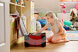 Little girl packing suitcase at home. Cute child putting clothes into suitcase. Preparing for family vacations with