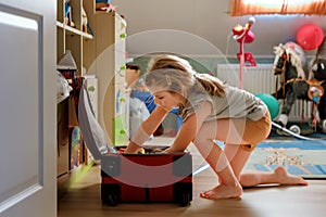 Little girl packing suitcase at home. Cute child putting clothes into suitcase. Preparing for family vacations with