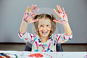 Little girl with painted colorful watercolor hands up, child sitting at the table and drawing,