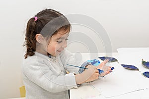Little child painting leaves blue, arts and crafts. Classic leaf painting art. Child paints her own hand with blue paint