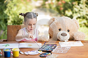 Little girl painting outdoor with her teddy bear friend