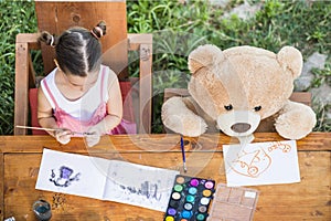 Little girl painting outdoor with her teddy bear friend