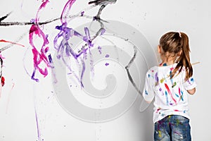 Little girl painting a white wall with colorful paint.