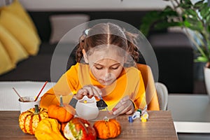 A little girl paints a clay hand made pumpkin. Halloween party. Crafts for children