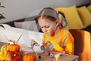 A little girl paints a clay hand made pumpkin. Halloween party. Crafts for children