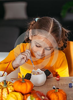 A little girl paints a clay hand made pumpkin. Halloween party. Crafts for children