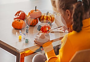 A little girl paints a clay hand made pumpkin. Halloween party. Crafts for children