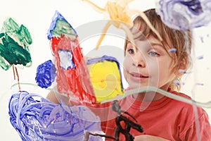 Little girl paints on glass, house, tree