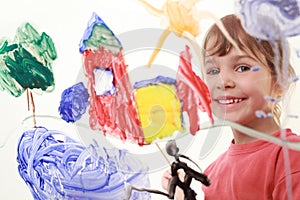 Little girl paints on glass and smiles