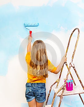Little girl paints the wall standing on a ladder