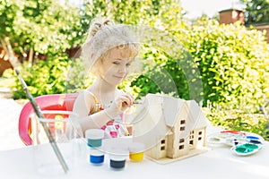 Little girl paints wooden model of house