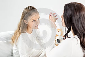 Little girl in pajamas looking at mother with cosmetic mirror