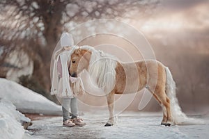 Little girl with palomino miniature horse in winter park