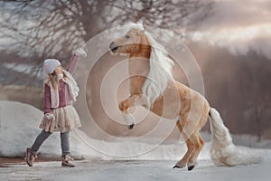 Little girl with palomino miniature horse in winter park