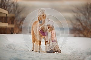 Little girl with palomino pony in winter park