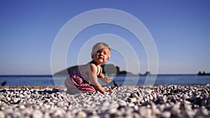 Little girl with a pancake in her hand gets up and walks along the pebble beach