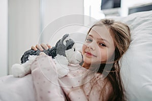 Little girl patient lying in hospital bed. Children in intensive care unit in hospital with plush toy.