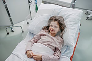 Little girl patient lying in hospital bed. Children in intensive care unit in hospital smiling.
