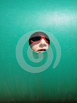 Little girl peeking through hole in green wall