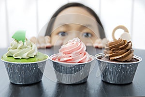 Little girl is peeping tasty cupcakes