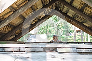 A little girl peers curiously from beneath an A-frame wooden roof, blending with nature's tranquility, and childhood