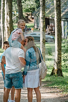 A little girl perches atop her father& x27;s shoulders, as the family enjoys a peaceful day at the park, the essence of