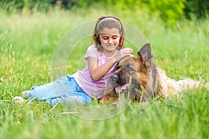 Little girl petting shepherd dog sitting in the grass