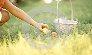 Little girl picking in basket colorful painted eggs on Easter egg hunt in park