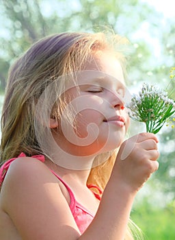 Little girl picking summer flowers in a field. Happy child enjoying nature outdoors. Sunlit  little girl smelling summer flowers