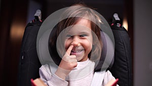 little girl picks her nose, the girl sits in a child's car seat