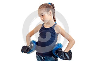 Little girl with pigtail stands sideways looks down and keeps her hands on the sides of the boxing gloves