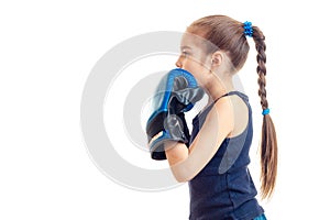 Little girl with pigtail stands sideways to the camera in boxing gloves