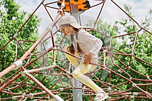 Little girl with pigtails and cap playing in rope polyhedron climb at playground outdoor having