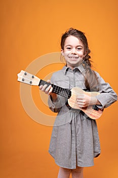 Little girl in pigtails are holding a small guitar in their hands while standing on a bright background