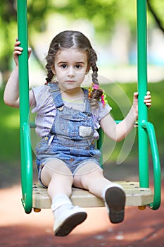 Little girl with pigtails sitting on a swing at