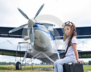 A little girl in a pilot`s costume sits on a retro suitcase at the airport waiting for the departure of the flight. A