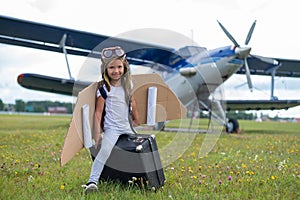 A little girl in a pilot`s costume sits on a retro suitcase at the airport waiting for the departure of the flight. A