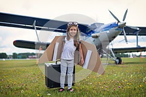 A little girl in a pilot`s costume sits on a retro suitcase at the airport waiting for the departure of the flight. A