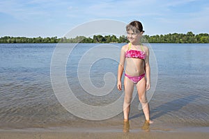 Little girl in a pink bathing suit on the river, on a sunny, warm day