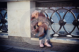 Little girl in a pink beret sits at a fencing of the bridge