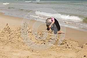 Little girl in pink and black wetsuit making sand castles