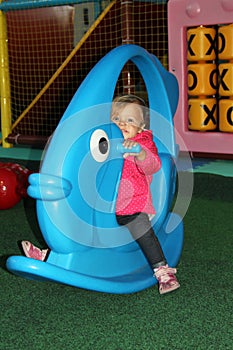 little girl in pink coat swinging on a blue toy in the form of f