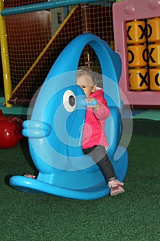 little girl in pink coat swinging on a blue toy in the form of f