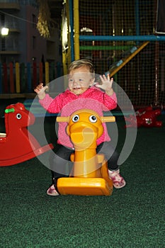 little girl in pink coat swinging on a yellow toy in the form of